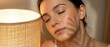 © Оксана Алищук - Woman with dark hair and olive complexion relaxing near warm lamp light, eyes closed in peaceful moment. Suitable for wellness, skincare, relaxation and lifestyle content.