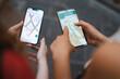 © Studio Marmellata - Two female travelers hold up their smartphones side by side to compare digital map navigation routes while searching for directions on a cobblestone street.