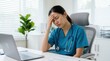 © Masque - Tired healthcare worker experiencing a headache and fatigue while sitting at a desk.