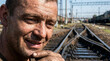 © Bluum - Portrait of a railway worker looking at the camera. Man with dirty face working on industrial train tracks. Infrastructure maintenance, heavy labor and engineering industry career