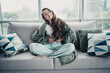 © deagreez - Young woman sitting on sofa clutching her stomach in pain at home, showing abdominal discomfort and distress