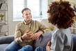 © Studio Romantic - talking on sofa at home, conversation. Smiling man listens to woman in a bright living room, showing relationship trust and empathy. Clear concept is communication at home.