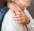 © Ирина Гутыряк - A young woman's hand holds the hand of a senior adult man, comforting or sympathizing with him. Concept of Caregiver Support and Home Care