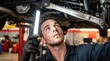 © Taras Roshchuk - A man is working under a car in an auto repair shop. He holds a light while checking the car's parts. Tools and equipment are visible in the background