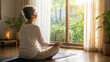 © Teeradej - Elderly Asian woman sitting cross-legged in meditation on a mat by a sunlit window. Stress reduction and longevity mindfulness concept.
