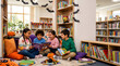 © TaZJunG - Diverse group of children reading books in a decorated library for Halloween.