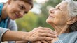 © waragron - A young caregiver gently holds an elderly woman's hand, sharing a warm and compassionate moment outdoors.