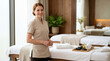 © Len_mik - Smiling female massage therapist in a beige uniform. Professional masseuse standing by a massage table with hot stones and oil in a modern spa room