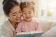 © polack - Asian woman and a child are sitting on a couch reading a book together. The woman is smiling and the child is smiling as well. Scene is happy and warm, as the mother