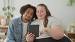 © Krakenimages.com - Plus size woman and man sit close on bed, smiling, woman points finger and man taps tablet screen in building bedroom; togetherness joy.