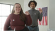© Krakenimages.com - Woman with voted sticker smiles and waves hand while man stands behind near ballot box in building; pride civic duty.