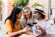 © Xavier Lorenzo - Three young women friends drinking red wine outdoors at cafe table. Multiracial female friends enjoying friendship and leisure in Europe. Lifestyle and travel concept.