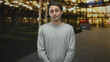 © Krakenimages.com - Man in gray sweater with hands clasped then touching chest and pointing finger at camera in front of building entrance at night; thoughtful reflection.