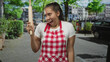 © Krakenimages.com - Woman cook smiling with eyes closed holds rolling pin upright on city street wearing red checkered apron and white tee; culinary joy.