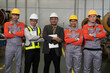 © amorn - Group of workers, manager, and engineer standing together with crossed arms in industry factory, wearing safety uniform and helmet. Factory workers working in factory