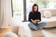© gzorgz - Full length of a brunette haired young woman reading a book in her modern home