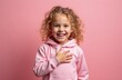 © miss irine - Little girl with blonde curly hair wears pink hoodie. She smiles brightly with hand on chest, making gesture for promise or oath. Isolated studio shot.