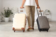© Pixel-Shot - Man in casual attire pulling two suitcases in a bright hotel room, travel and vacation concept, Preparation for a journey or the arrival at a destination