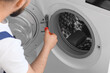 © Pixel-Shot - Professional repairman fixing a washing machine door with a screwdriver, home appliance maintenance and service concept, the technician is focused on the task