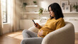 © Stocky Boi - Pregnant woman relaxing at home, comfortably sitting on a chair and using her smartphone.