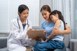 © M+Isolation+Photo - Female doctor talking with a mother while examining her sleeping daughter on a sofa in a clinic, family healthcare consultation and care