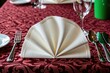 © Viktor - Elegant restaurant table setting with white napkin folded like fan on deep red tablecloth. Shiny metal cutlery including fork spoon knife arranged beside crystal glasses. Pro catering service place