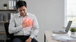 © Yuparet - Health concerns can cause discomfort in workplace as man experiences chest pain while sitting at desk with laptop and documents in modern office environment