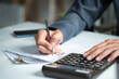 © winnievinzence - Accountant hand using a calculator and writing on financial expense receipt documents at an office desk, representing tax calculation and auditing
