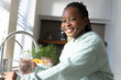 © Wavebreak Media - Female youth smiling, holding glass by stainless faucet at kitchen sink wearing pale green hoodie