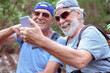 © luciano - Senior male friends enjoying active retirement, capturing happy moments with a smartphone selfie while hiking outdoors, embracing technology and friendship
