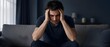 © Sumariyaniie - Depression, stress and man on couch at home with anxiety, headache and mental health problems. Sad person, pain and migraine in living room with burnout, frustrated face, loneliness and despair