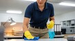 © Bilal Ulker - Cleaning Professional at Work: A diligent cleaner wearing yellow gloves and a blue polo shirt meticulously wipes down an office desk with a spray bottle and cloth, ensuring a spotless workspace.