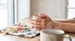 © Rendara Studio - Close up of hands cradling steaming ceramic mug on floral cloth by bright window