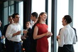 © ultramansk - A lively business networking crowd, mingling and laughing at the reception at a bright hotel reception by the windows, for a polished travel tourism and lifestyle theme.