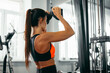 © Sergio - A woman focuses on her workout while using a cable machine in a gym. She pulls down on the handles, engaging her upper body as part of her fitness routine