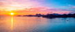 © yuvaraj - Panoramic sunset landscape featuring a vibrant golden sun over calm tropical ocean waters with distant mountainous islands under a dramatic colorful sky at dusk time