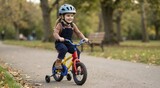 Happy young girl riding a colorful bicycle with training wheels in a park. Child wearing a safety helmet learning to cycle on an autumn day
