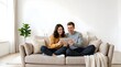 © Giulia - Happy couple sitting on sofa at home laughing while using a tablet