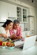 © Marko Geber - Man and woman cooking together with laptop in home kitchen