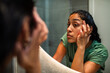© Marko Geber - Woman examining eye area in bathroom mirror