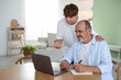 © New Africa - Caregiver. Teenager helping senior man learn how to use laptop indoors, space for text