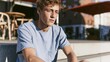 © Lifestyle Images - Portrait of a young man sitting on a concrete bench. he is wearing a light blue t-shirt and has short blonde hair. he has a serious expression on his face and is looking directly at the camera.
