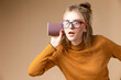 © danmorgan12 - Curious Caucasian Blond Girl Listening To Hidden Gossips Secrets Using Disposable Paper Drinking Cup On Beige as Hearing Medical Concepts.