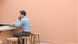 © joeycheung - Man enjoys burger at counter, seated on stool against peach-colored wall.