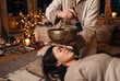 © DH - A woman lying peacefully while receiving a relaxing sound healing therapy session with a Tibetan singing bowl in a cozy, candlelit room.