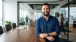 © Ayesha - Friendly bearded man leaning on a conference table in an open plan office