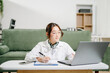 © Nuttapong punna - Asian woman manages business calls on her smartphone while working on a laptop with documents at home, blending corporate flair with cozy remote work.