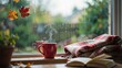© Streamline Design - Red steaming cup of hot coffee or tea on a window sill with plaid blanket and open book, autumn leaves outside rainy window.