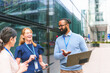 © pablo - Diverse business professionals having a casual outdoor meeting while discussing projects and using technology