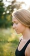 © Undersea - Young Caucasian woman with blonde hair in profile, wearing black tank top, eyes closed in peaceful expression outdoors during golden hour with blurred green nature background.